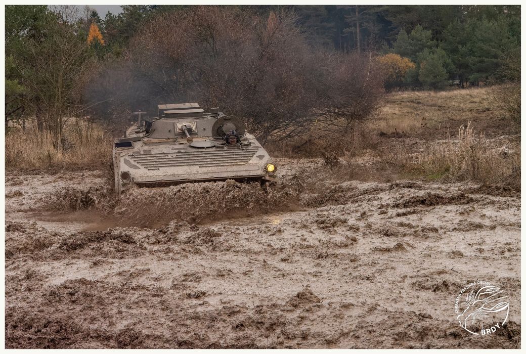 Bojové vozidlo pěchoty projíždí řídkým blátem na vojenském cvičišti.